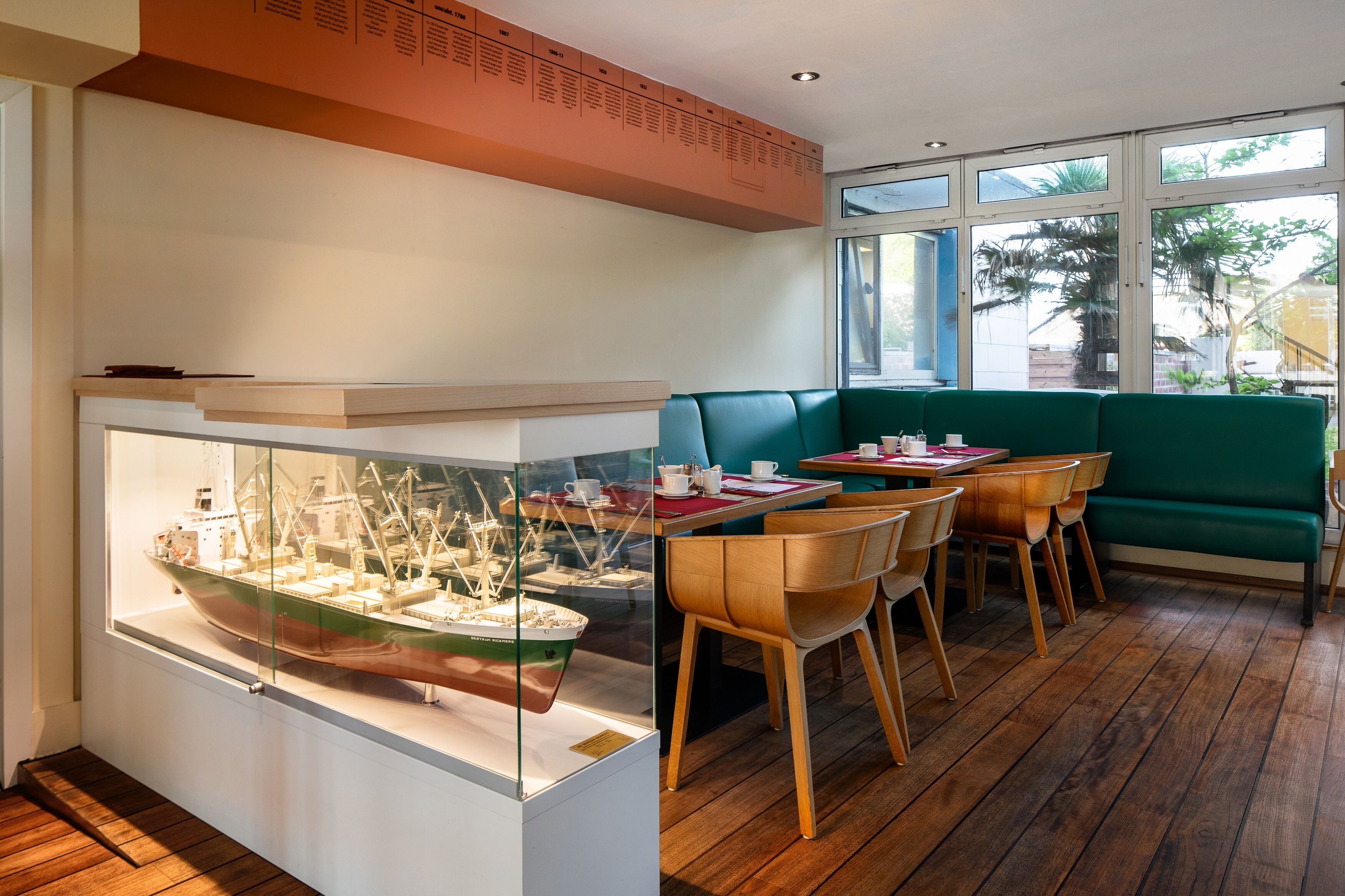 Ein Restaurant mit Holzboden, grünen Sitzgelegenheiten und einer Schiffmodell-Ausstellung.