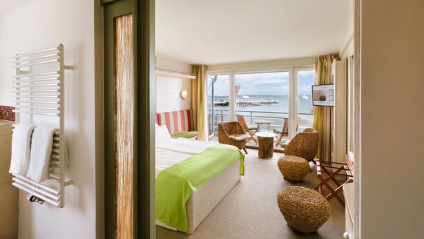 A hotel room with a bed, a seating area with chairs, a small table, and a view of the sea. - Hotel Rickmers Insulaner (Helgoland)