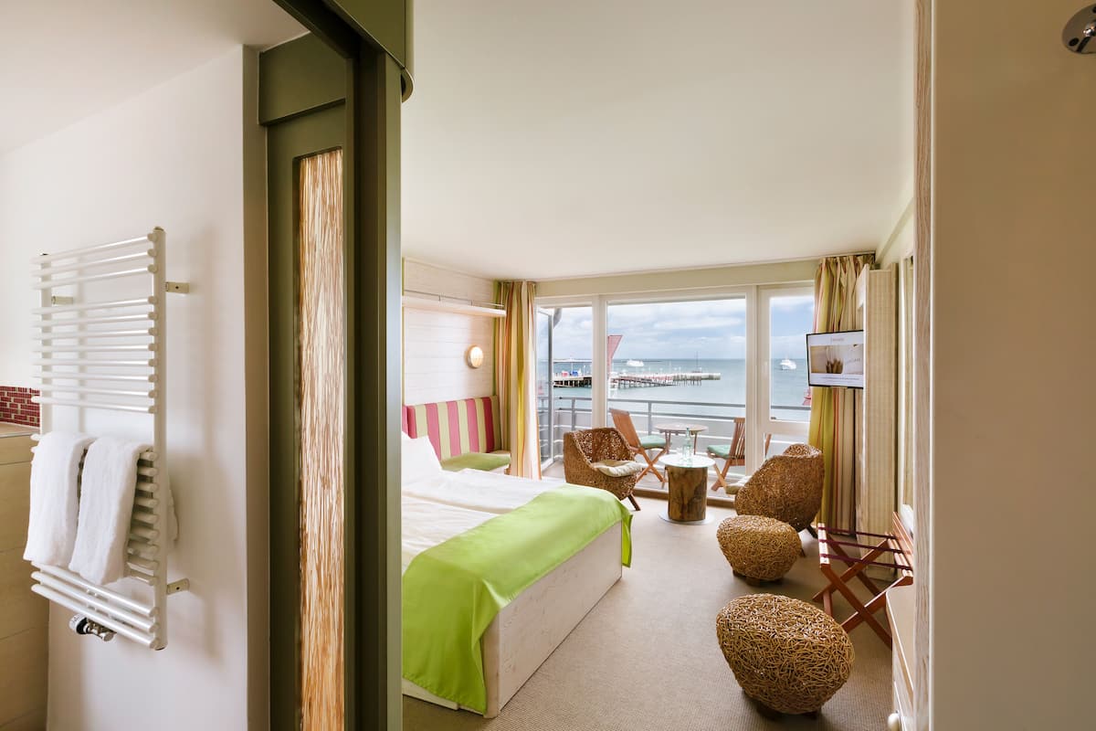 Une chambre d’hôtel avec un lit, un coin salon avec des fauteuils, une petite table et une vue sur la mer.