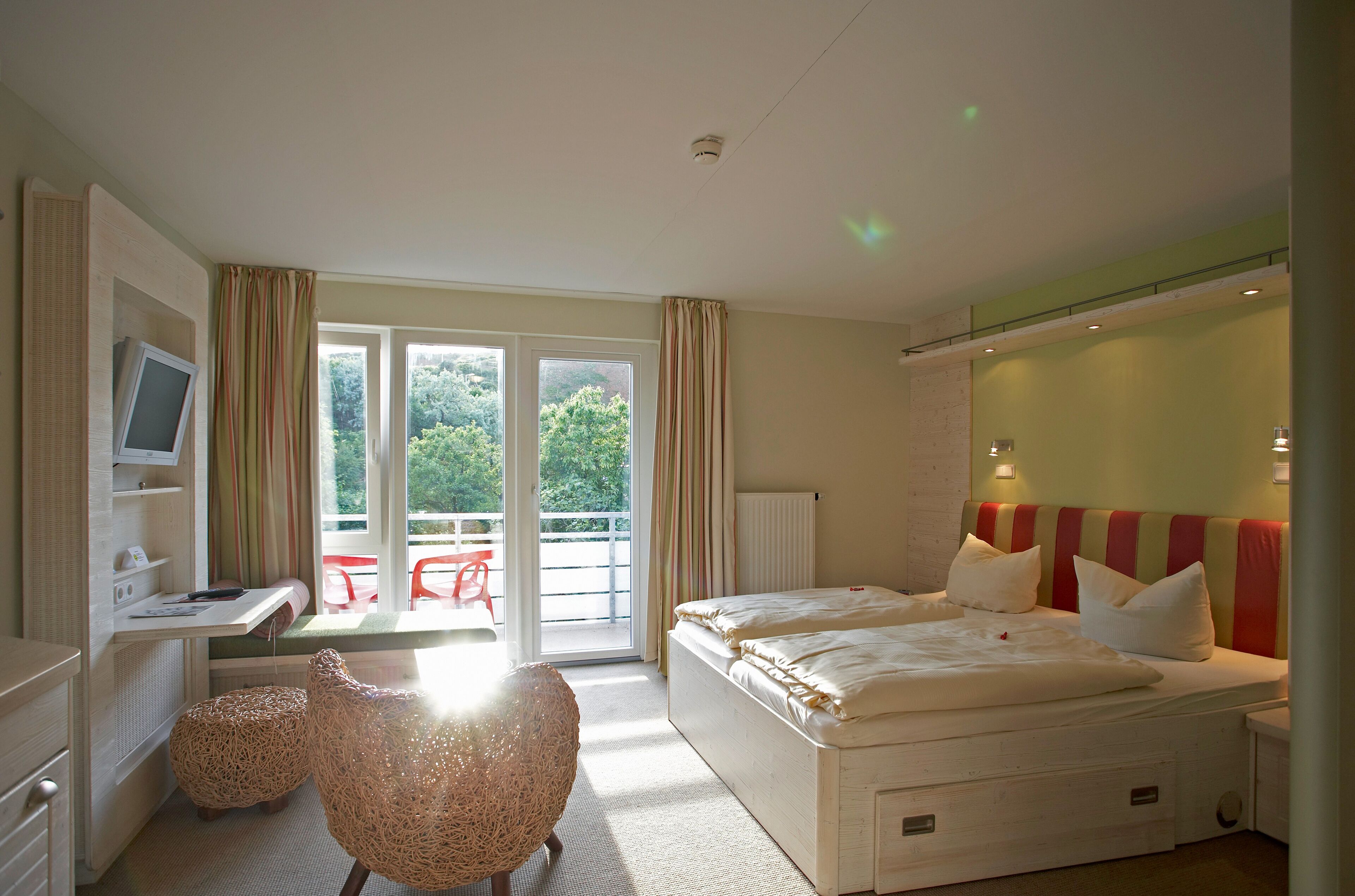 A bedroom with a bed, a desk, a chair, and a view of the outdoors.