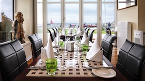 A dining area with a view of the sea, featuring a table set with green glassware and white napkins, surrounded by black leather chairs. - Hotel Rickmers Insulaner (Helgoland)
