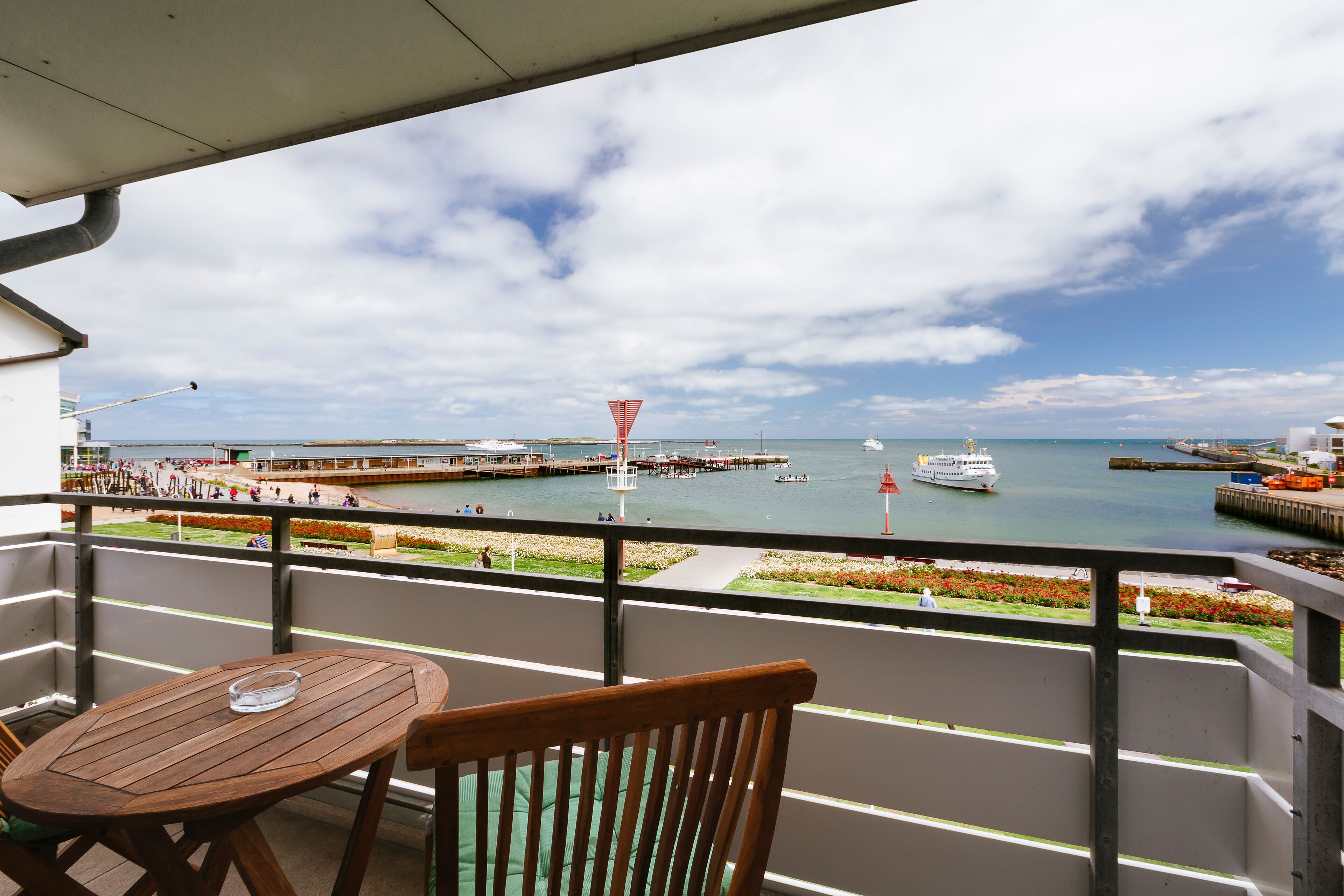 Een balkon met een houten tafel en stoel, met uitzicht op een jachthaven met boten en een steiger.