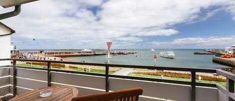 Een balkon met een houten tafel en stoel, met uitzicht op een jachthaven met boten en een steiger.