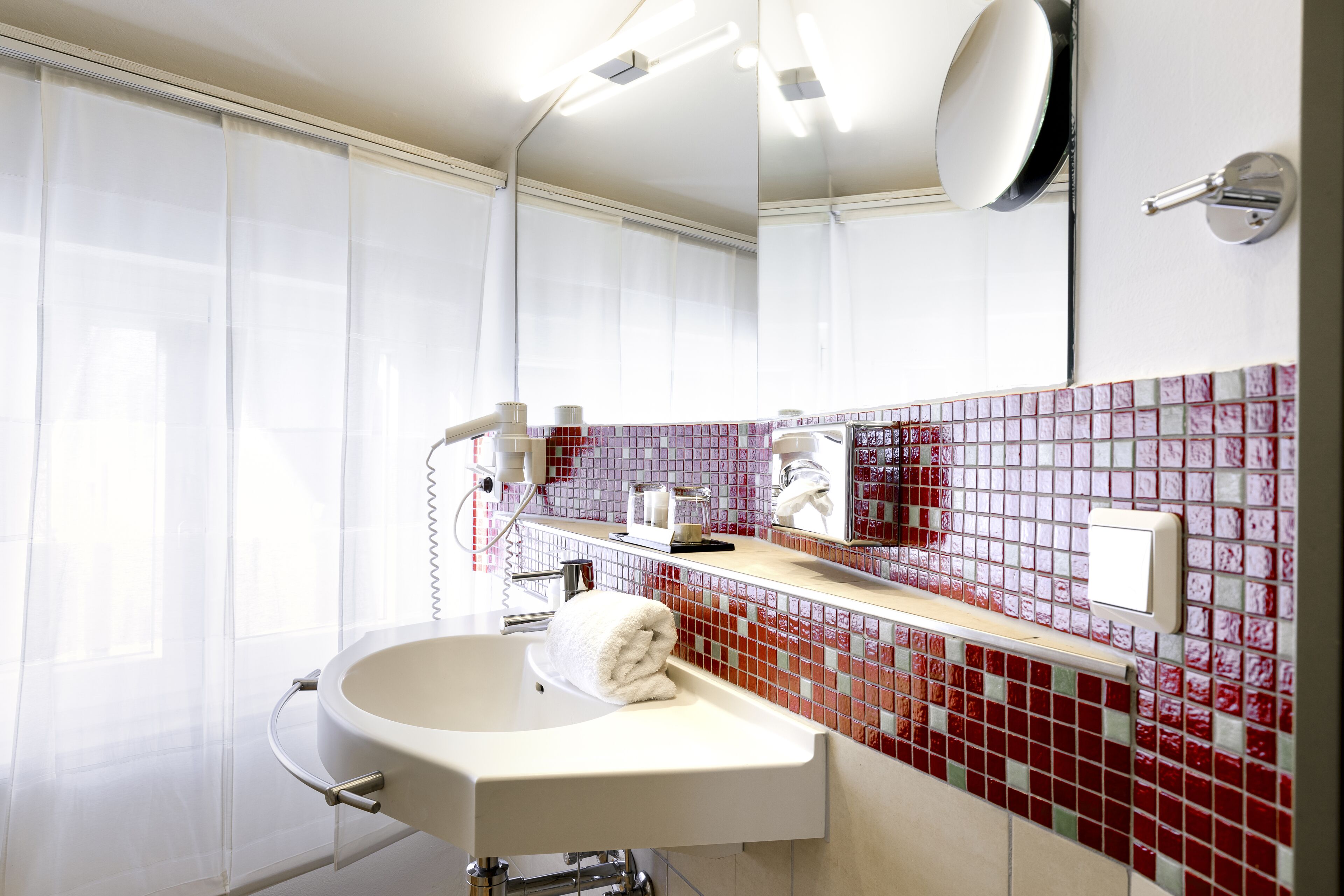 A modern bathroom with a white sink, a towel, a mirror, and a red-tiled backsplash.