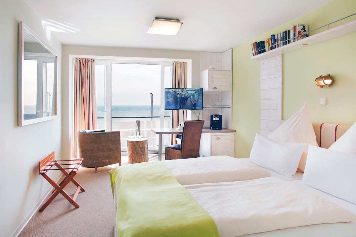 Une chambre d’hôtel avec un lit, un bureau, une chaise, une télévision et une vue sur la mer.