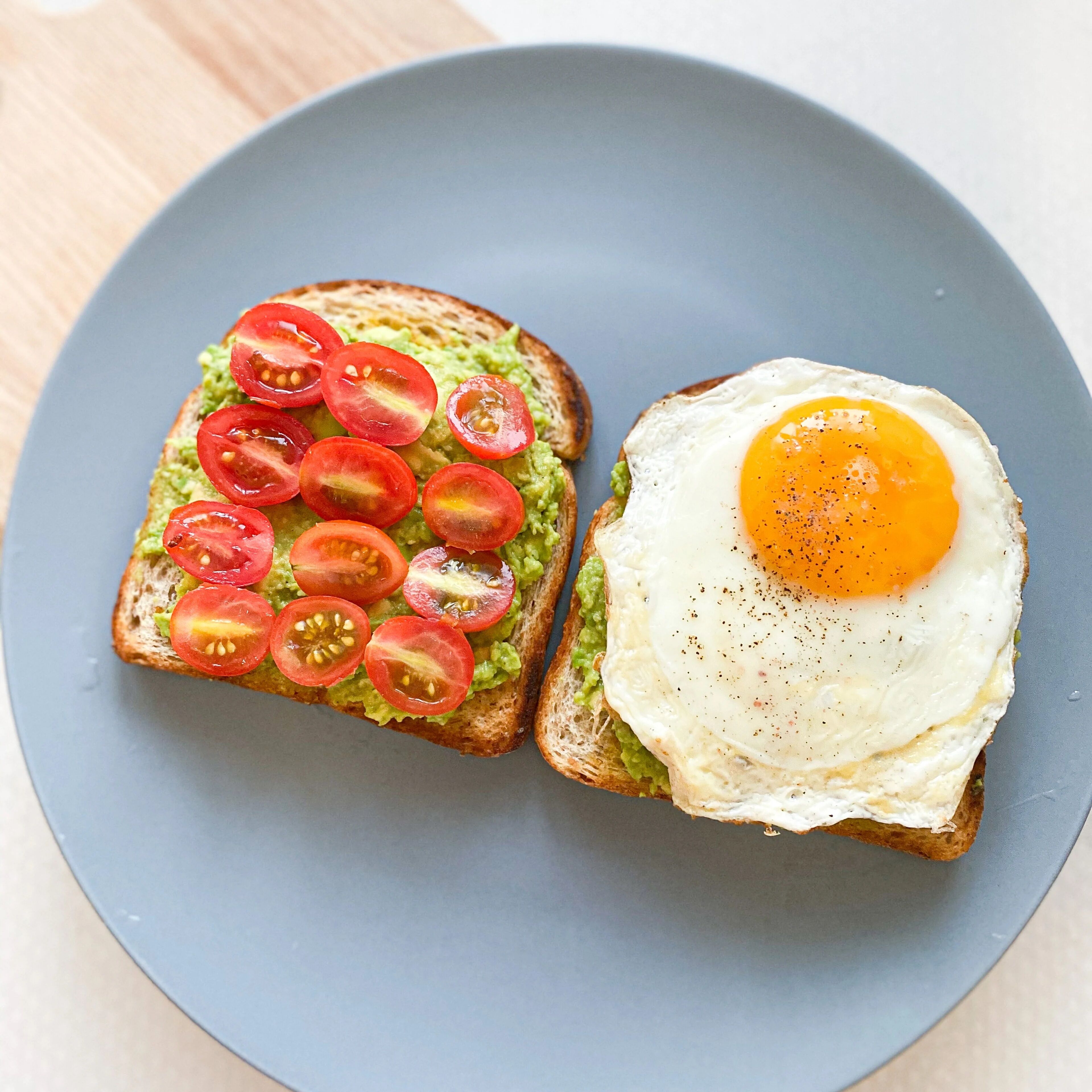 Zwei Toastscheiben, eine mit Avocado und Tomate belegt, die andere mit einem Spiegelei.