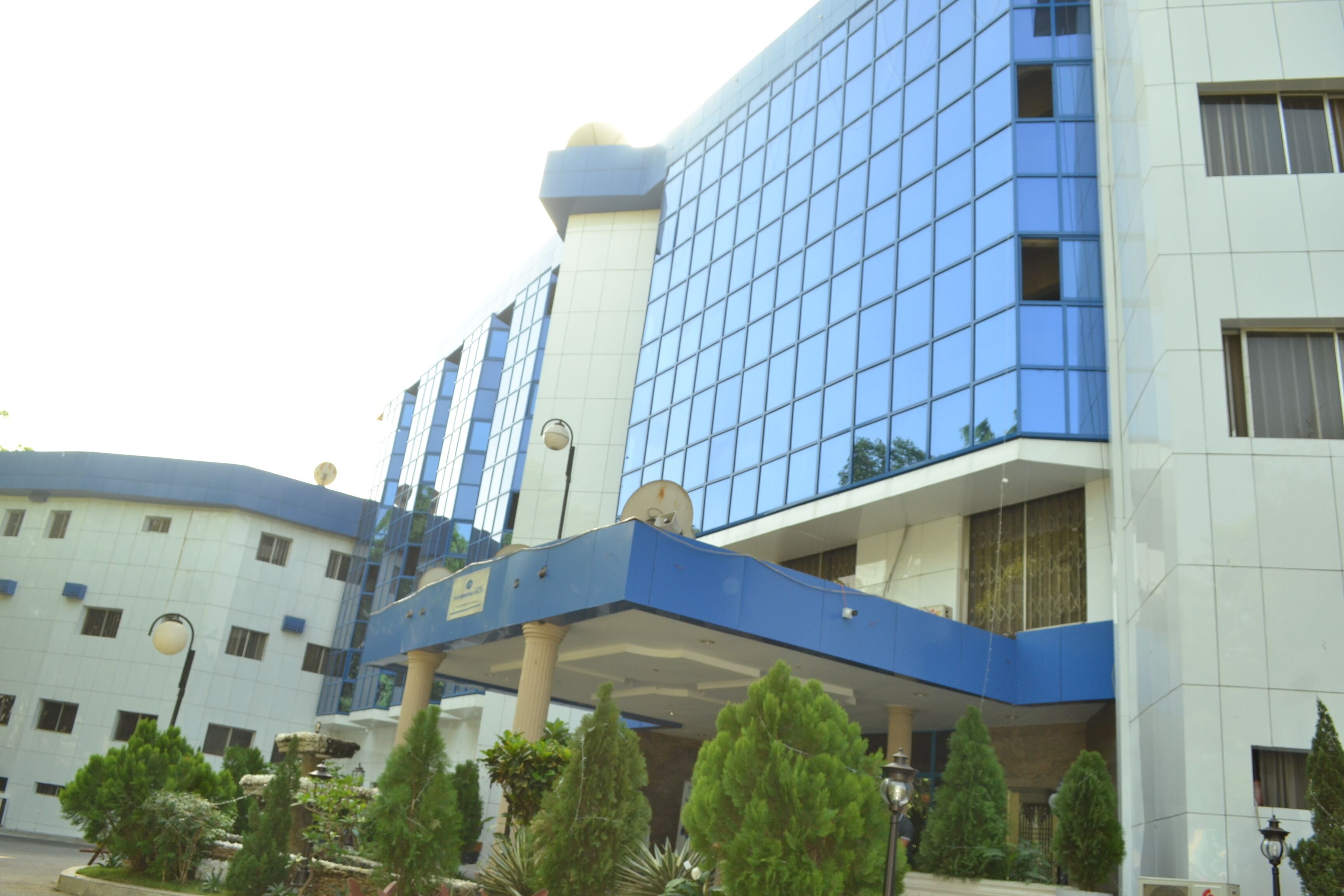 A modern hotel with a blue and white facade, multiple floors, and a covered entrance area with greenery.