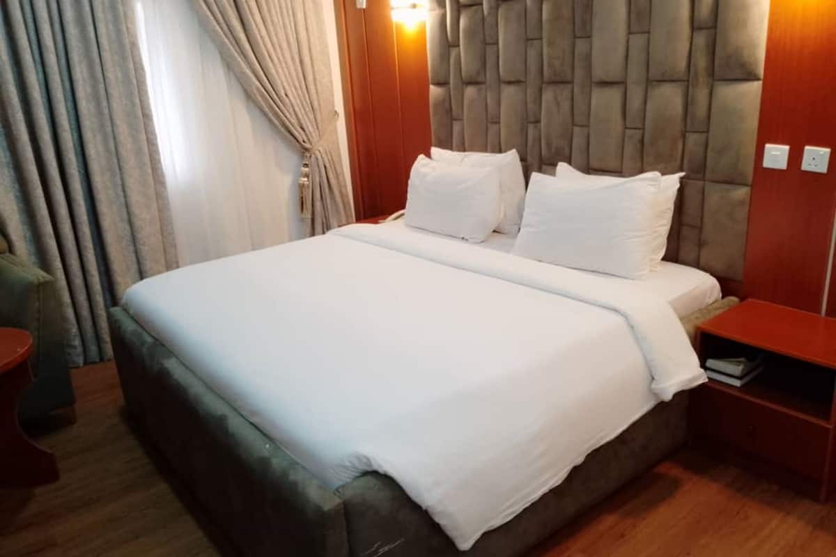 A hotel room with a large bed, wooden headboard, and a nightstand with a lamp.