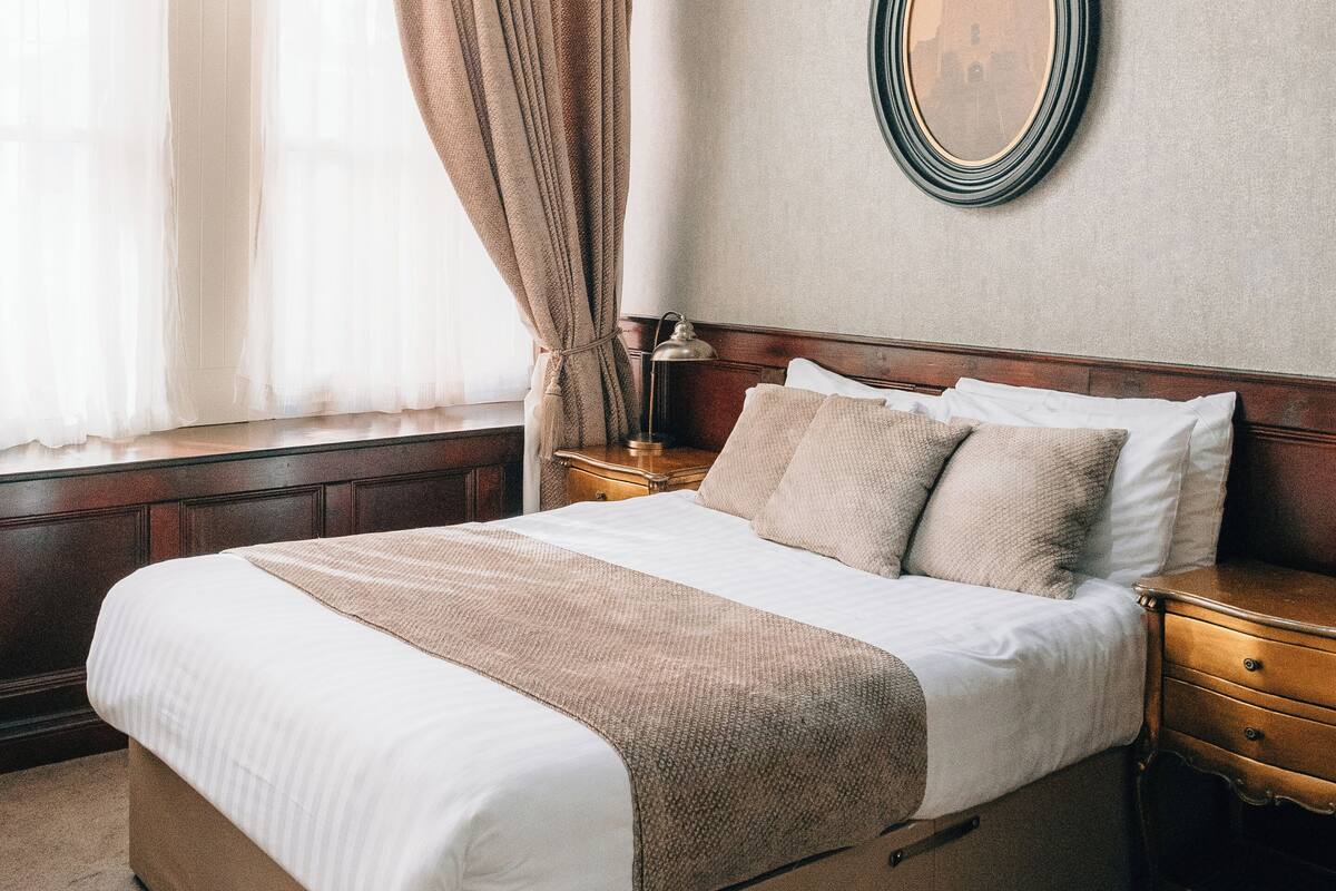 A neatly made bed with a wooden headboard, a bedside table with a lamp, and a large mirror on the wall.