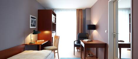A hotel room with a bed, desk, chair, and a large window.