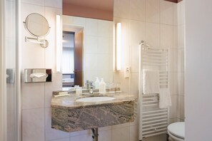 Un baño moderno con lavamanos de granito, un espejo redondo, un perchero y un inodoro.