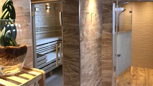 A modern sauna with wooden benches and a glass door, a wooden table with a glass bowl and green plants, and a textured wall. - Hotel Helgoländer Klassik (Helgoland)