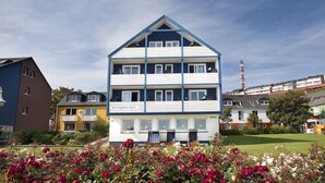 A multi-story hotel with a blue and white exterior, balconies, and a garden with flowers. - Hotel Helgoländer Klassik (Helgoland)