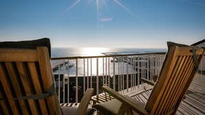 Two wooden chairs with cushions on a balcony overlooking a body of water with a bridge in the distance. - Hotel auf den Hummerklippen (Helgoland)