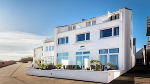 Un hotel moderno con fachada blanca, múltiples ventanas y un área de balcón con plantas en macetas.