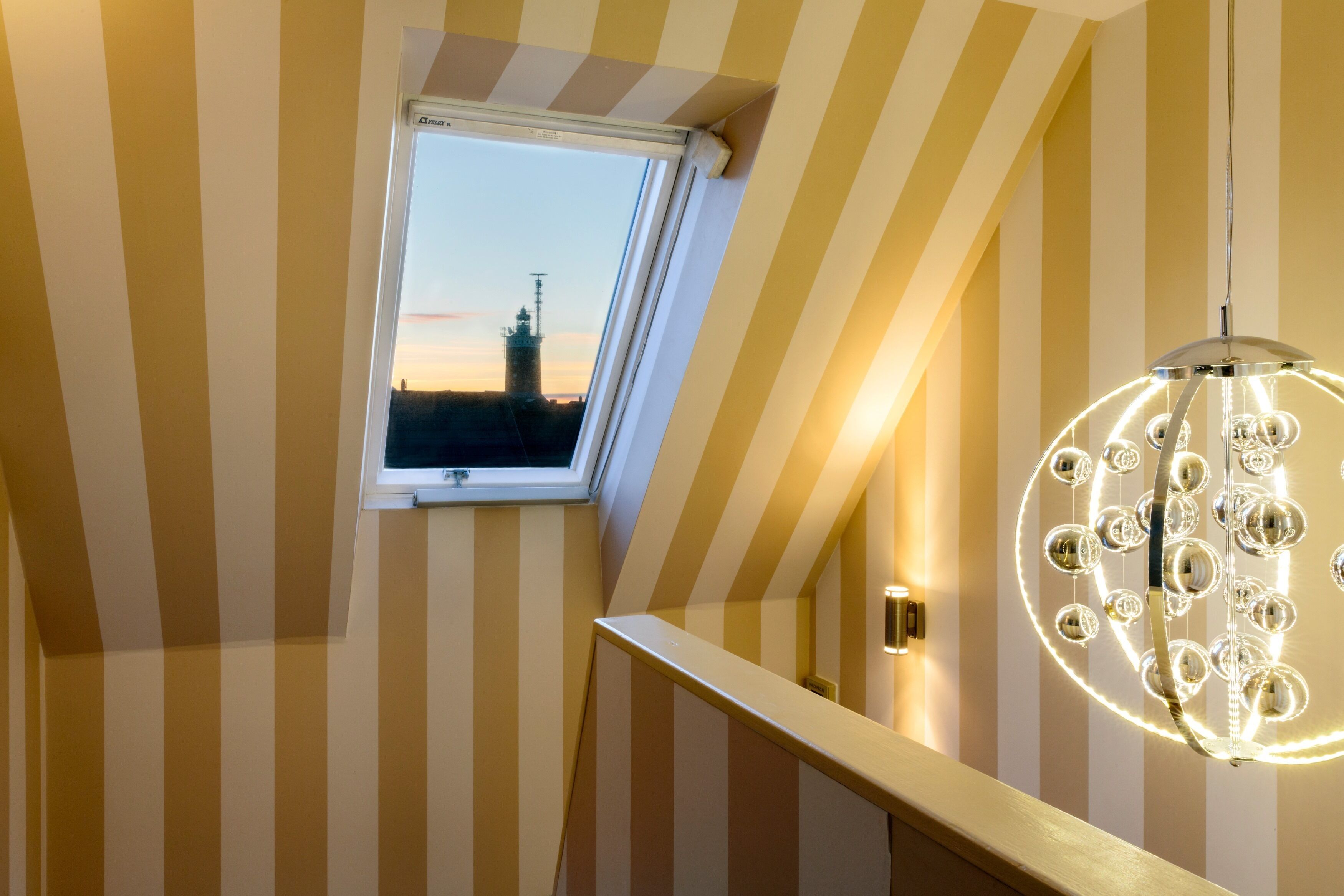 A staircase with striped walls and a skylight overlooking a cityscape at sunset.