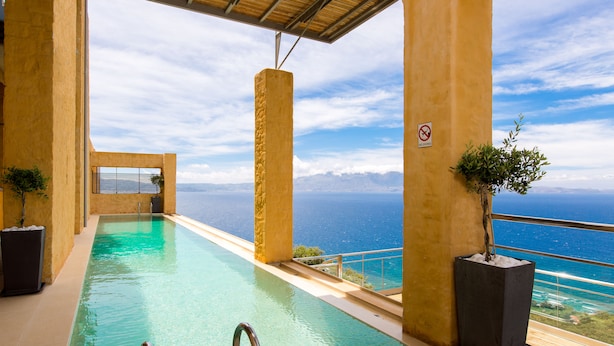 En infinitypool med fri utsikt över havet, omgiven av gula väggar och krukväxter.