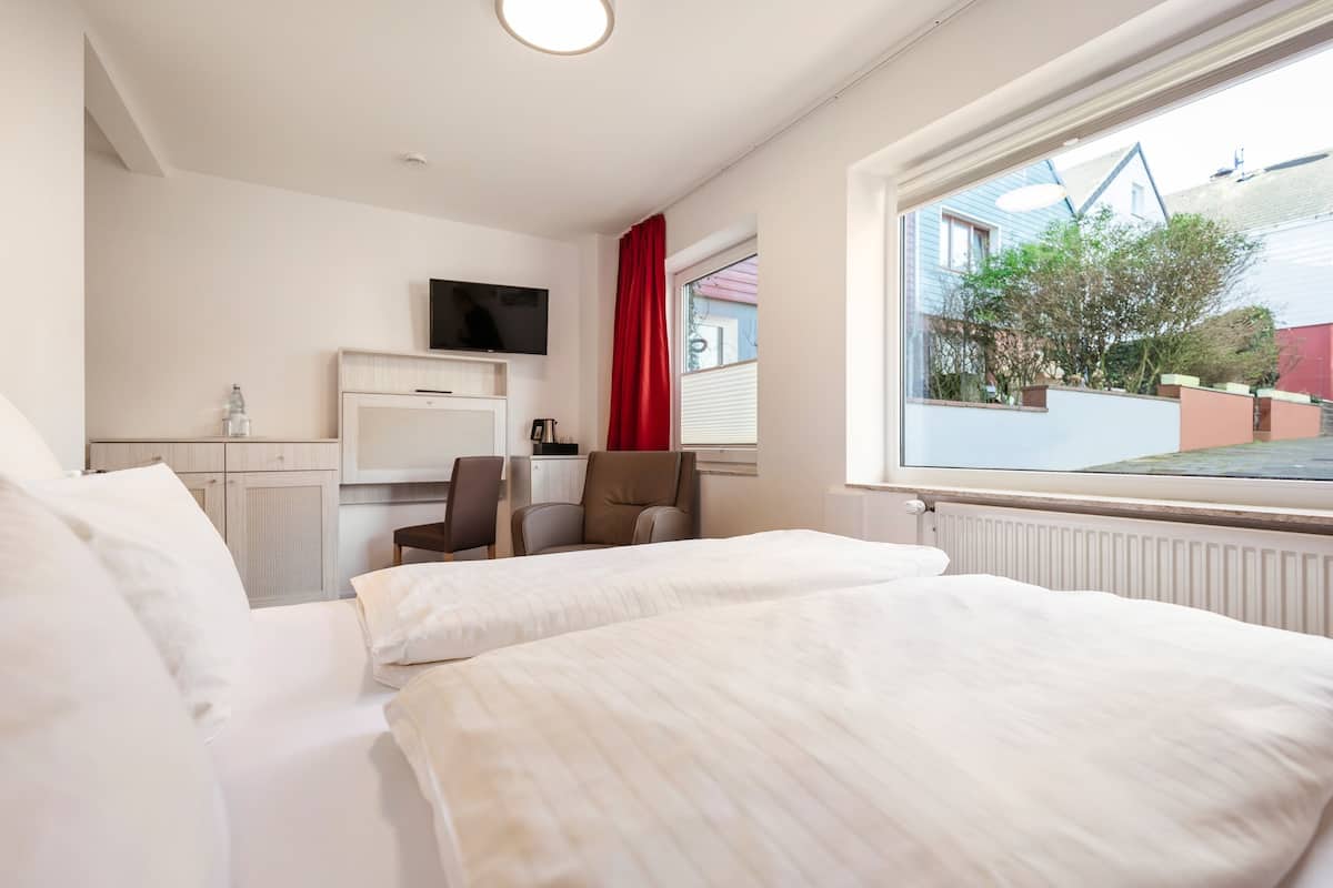 Quarto de hotel com duas camas, uma televisão fixada na parede, uma mesa com cadeira e uma janela com vista para o exterior.