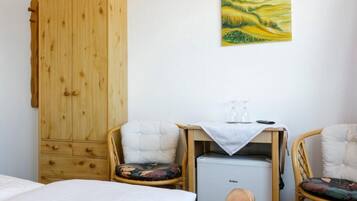Una habitación con un armario de madera, dos sillones tapizados con cojines, una mesita con una copa y una botella, y una cama con ropa de cama blanca.