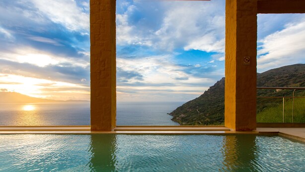 Una piscina infinita con vista al atardecer sobre el mar, enmarcada por pilares de piedra.