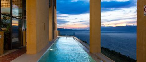 An infinity pool with a view of the sea at sunset.