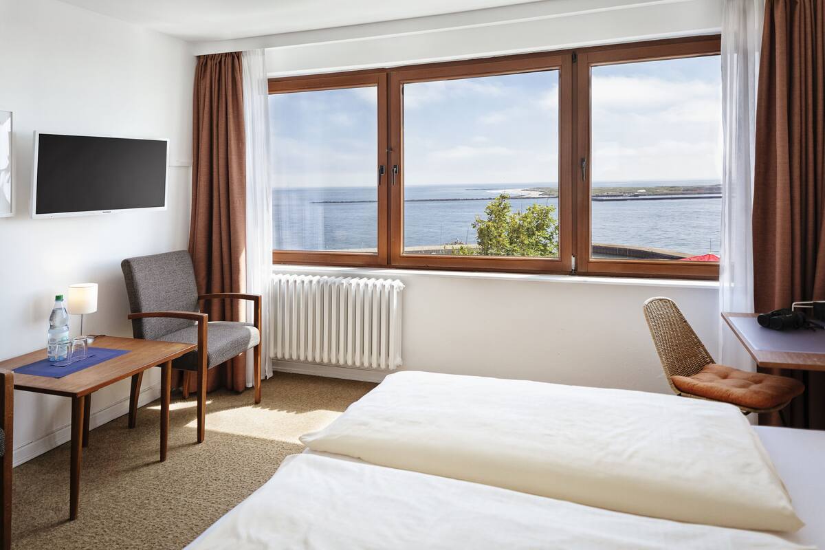 Quarto de hotel com cama, cadeira, mesa, televisão e janela com vista para o mar.