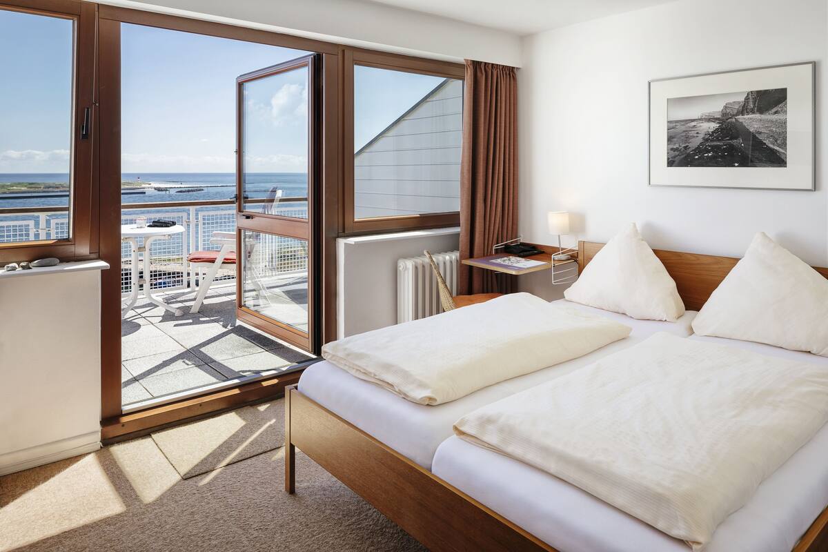 Quarto de hotel com cama, escrivaninha, cadeira, janela e vista para o mar.