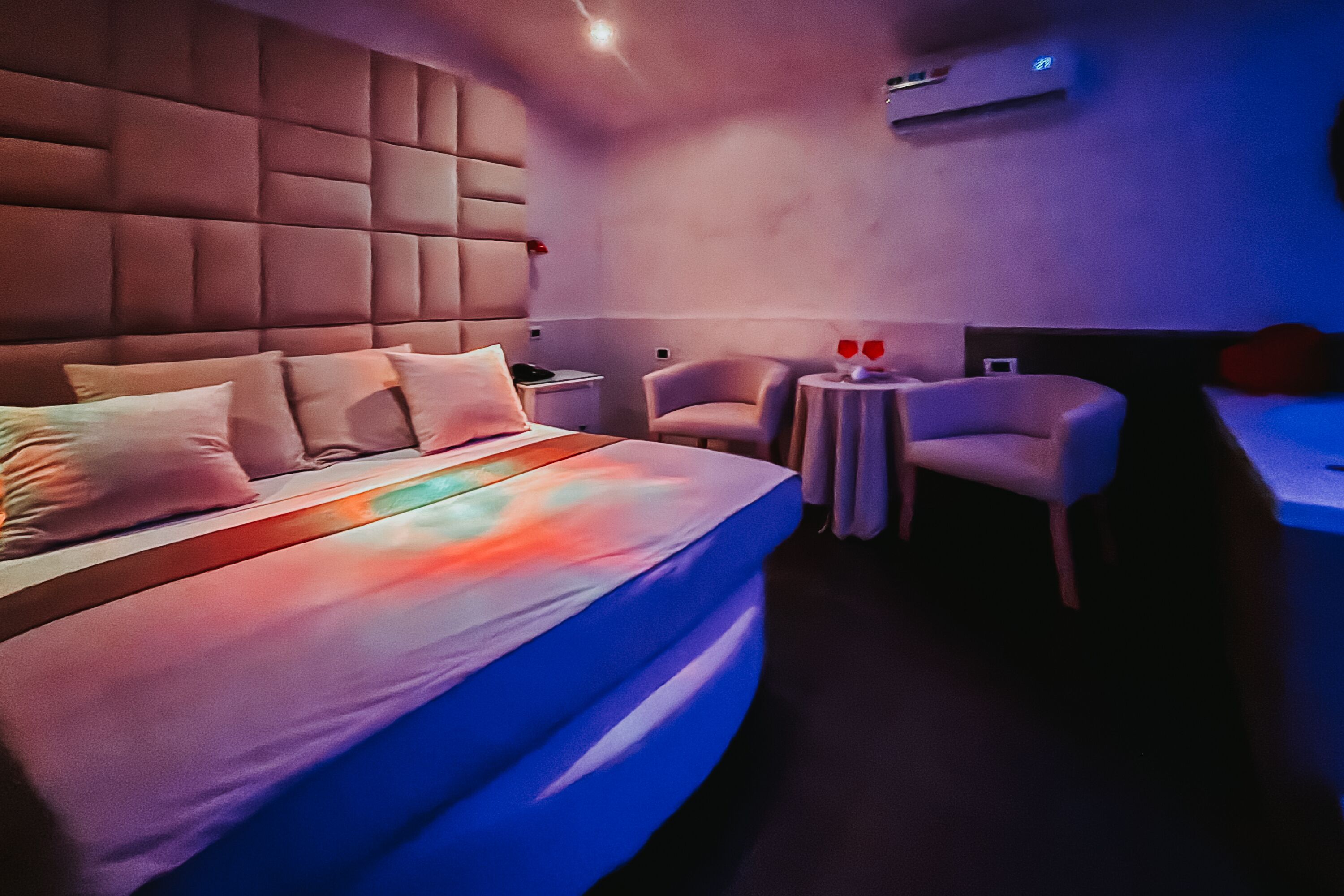 A modern hotel room with a large bed, two armchairs, a small round table, and a bedside table with a lamp.