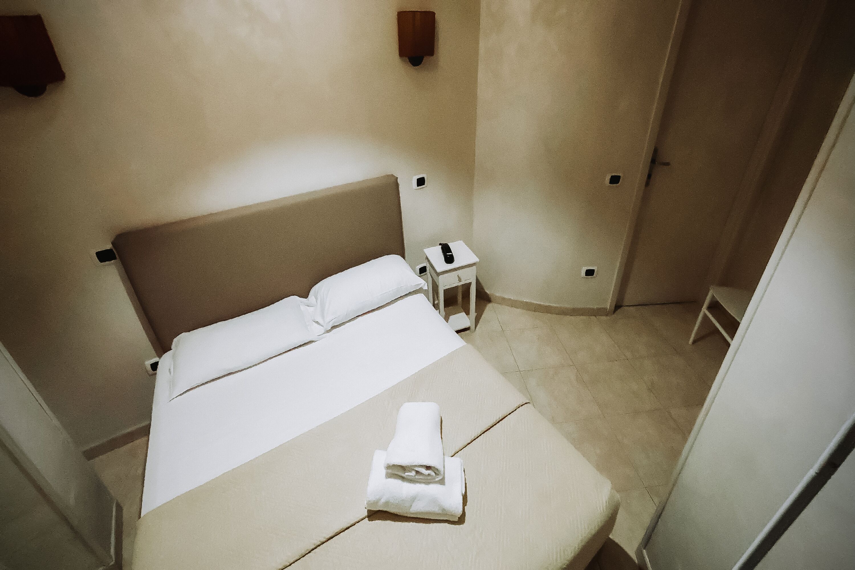 A small, clean hotel room with a single bed, a bedside table, and a nightstand.