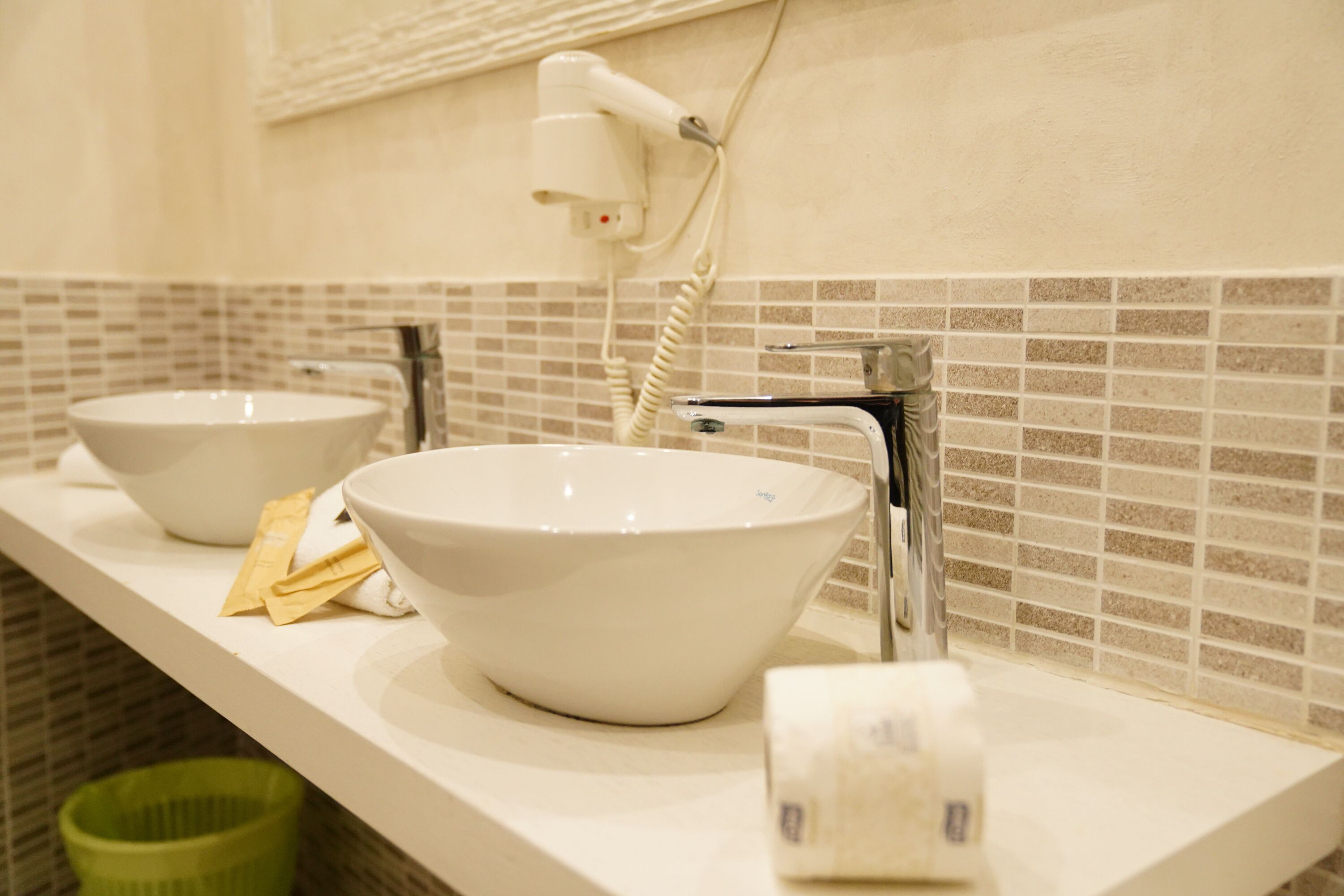 A bathroom with two sinks, a hairdryer, and a green trash bin.