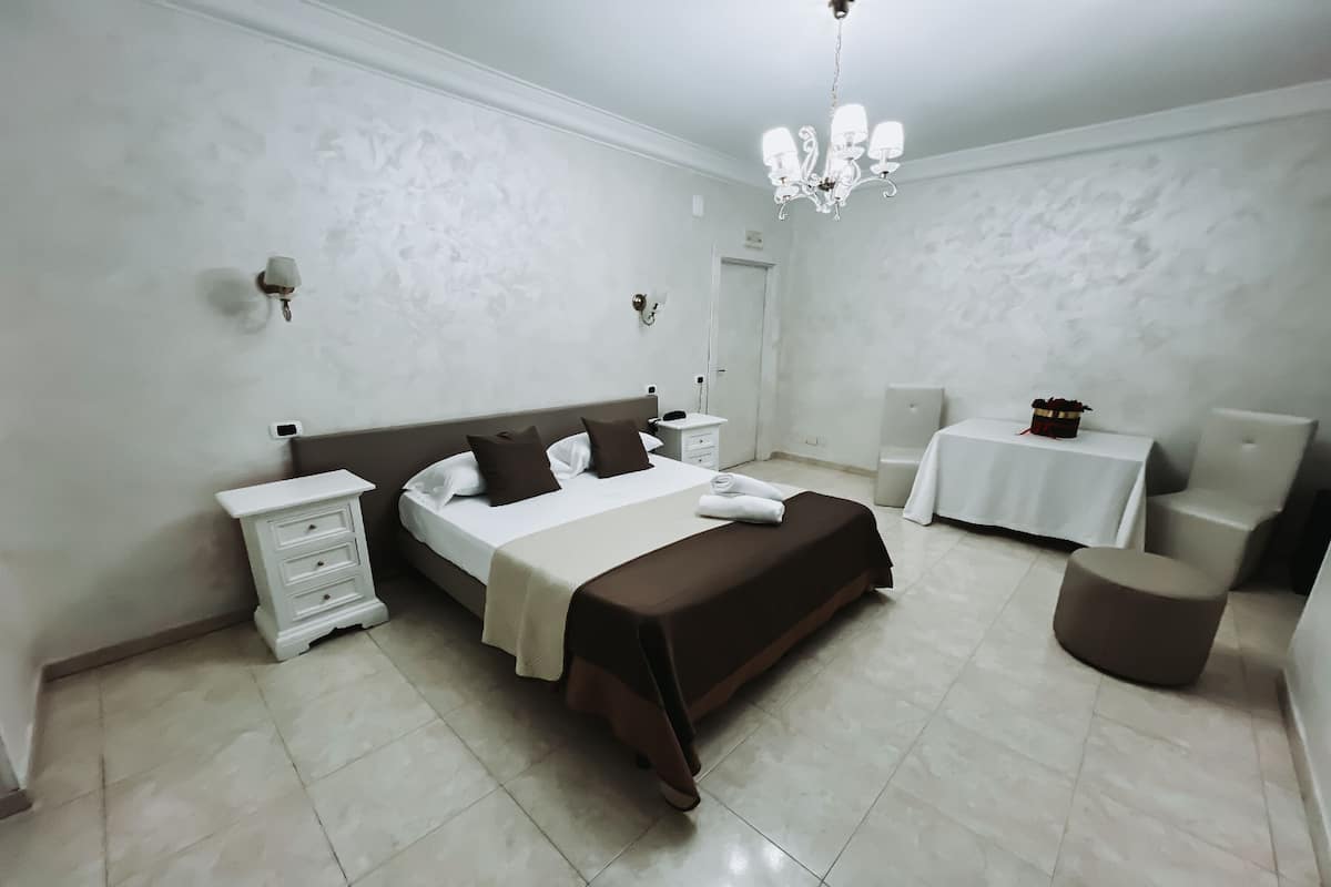 Quarto moderno com cama grande, mesas de cabeceira, uma pequena mesa e uma cadeira.