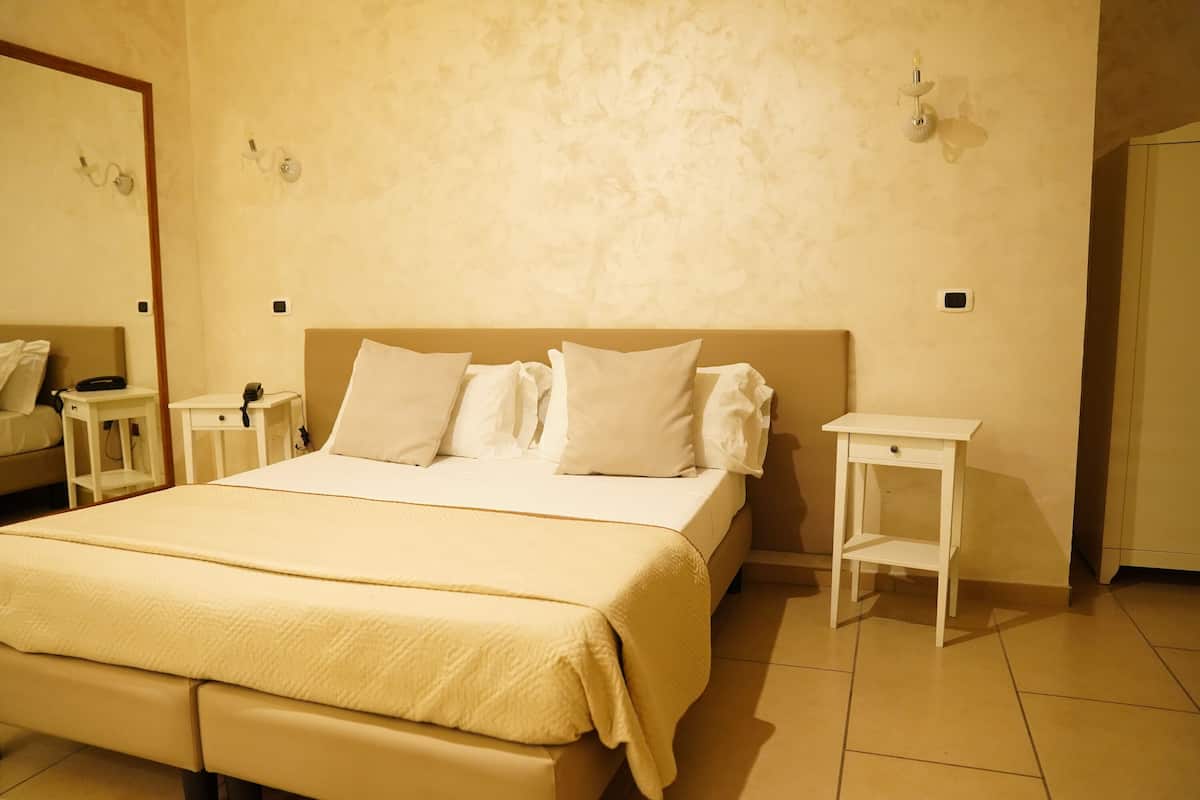 Quarto de hotel com uma cama grande, duas mesas de cabeceira e um espelho na parede.