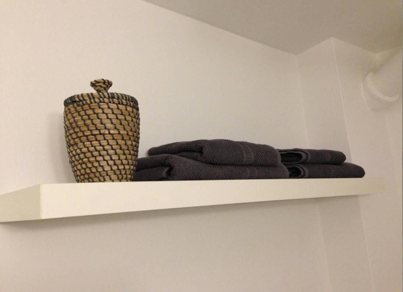 A white shelf with a woven basket and folded towels.