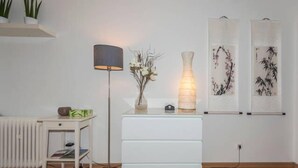 A minimalist room with a white dresser, a floor lamp, and two wall-mounted art pieces. - 1 bedroom apartment in prime location (Mannheim)