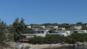 Uma área costeira com casas modernas à beira-mar, uma praia arenosa e um trecho de costa rochosa.