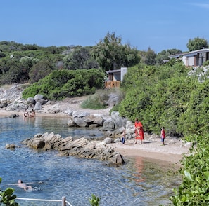 A coastal area with rocky terrain, a clear blue sea, and a few buildings with wooden decks.