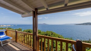 Um deck de madeira com cadeiras de lounge azuis, com vista para o mar costeiro.