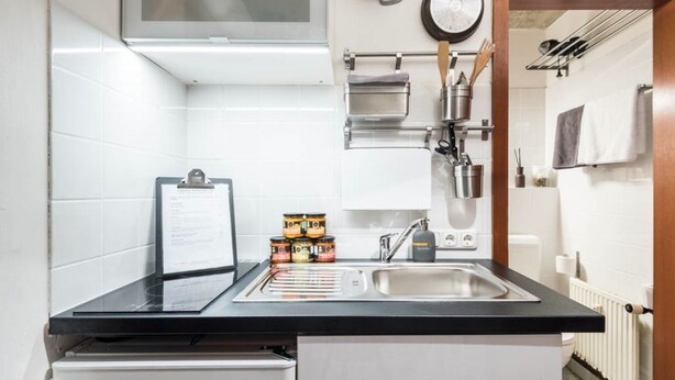 A modern kitchen with a black countertop, stainless steel sink, and a variety of kitchen utensils and appliances. - Charming Hipster Flat (Mannheim)