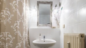 Een badkamer met een witte wastafel, een spiegel, een radiator en een douchegordijn.