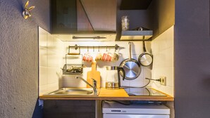 Een kleine keuken met een spoelbak, een fornuis en verschillende keukengerei dat aan de muur hangt.