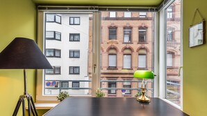 Une pièce avec une grande fenêtre, un bureau, une lampe et une chaise.