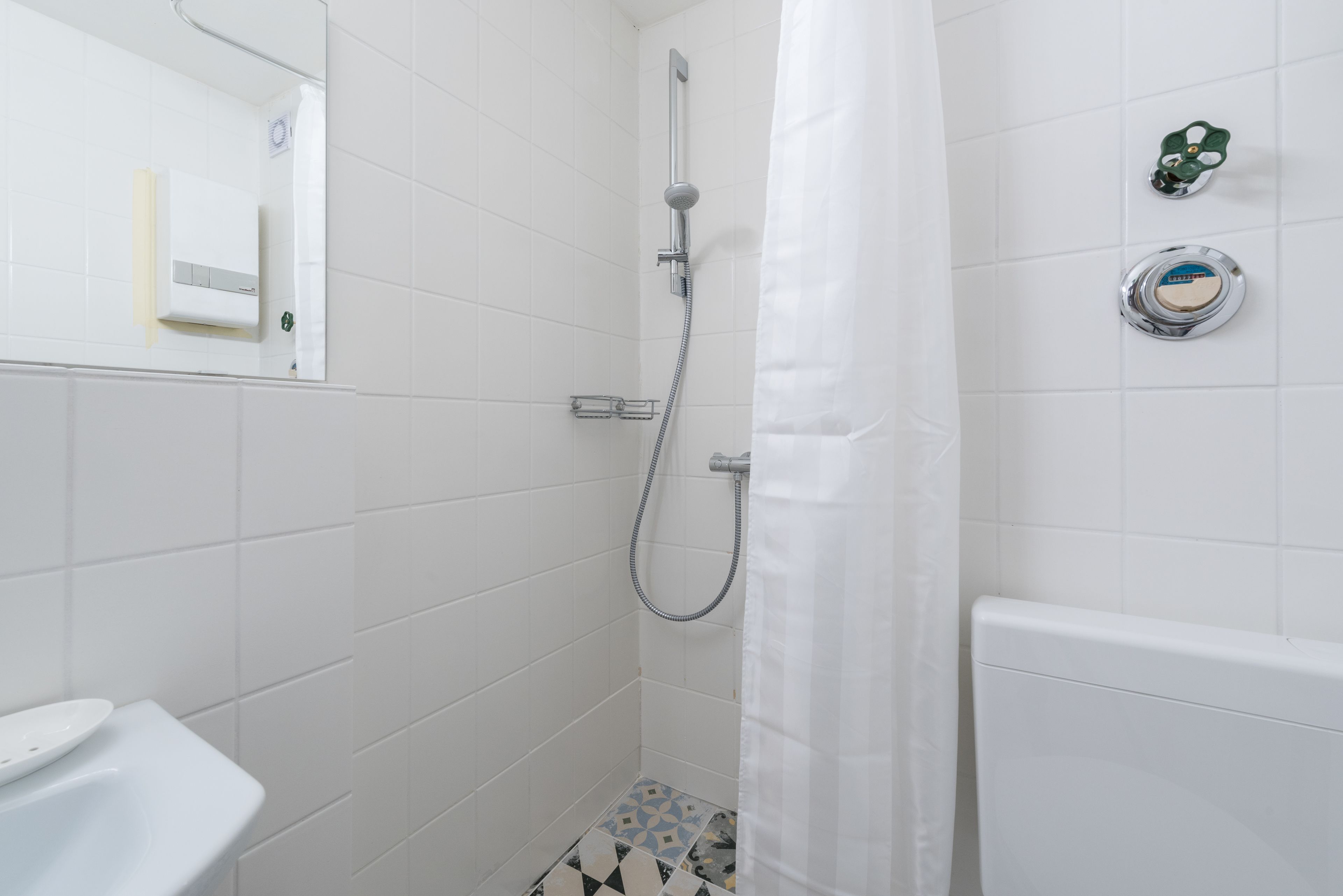 A bathroom with white tiles, a shower with a curtain, a toilet, and a sink.