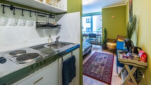 Une cuisine compacte équipée d’une cuisinière, d’un évier et d’ustensiles suspendus. On aperçoit un petit coin repas avec une chaise et une table.