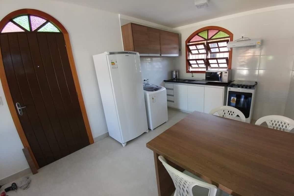 A compact kitchen with a refrigerator, stove, microwave, and sink. There is a wooden door with a window, and a dining area with a table and chairs.