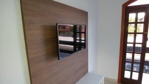 Una sala de estar moderna con un televisor de pantalla plana montado en una pared de paneles de madera, un banco blanco empotrado y un amplio ventanal hacia el exterior.