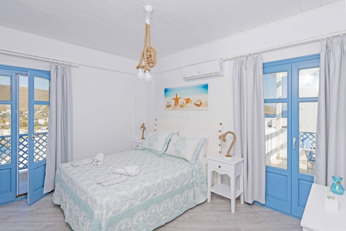 Ein Schlafzimmer mit einem Bett, einem Nachttisch, einem Fenster mit Vorhängen, einer Deckenleuchte und einer Wand-Klimaanlage.