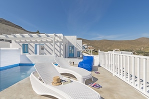 A rooftop pool area with white lounge chairs, a blue door, and a view of the surrounding landscape.