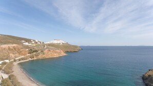 A coastal landscape with a white building complex on a hillside, a clear blue sea, and a winding road along the coast. - Aegean Sea Villas (Astypalaia)