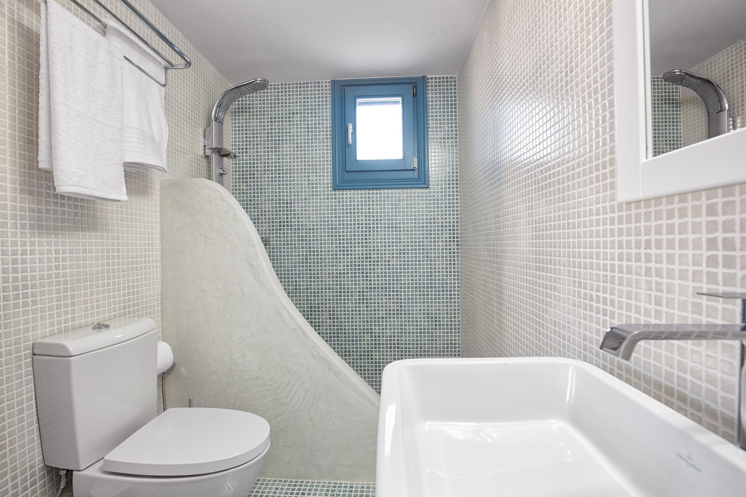 Un baño con inodoro y bañera blancos, y una zona de ducha con ventanal azul.