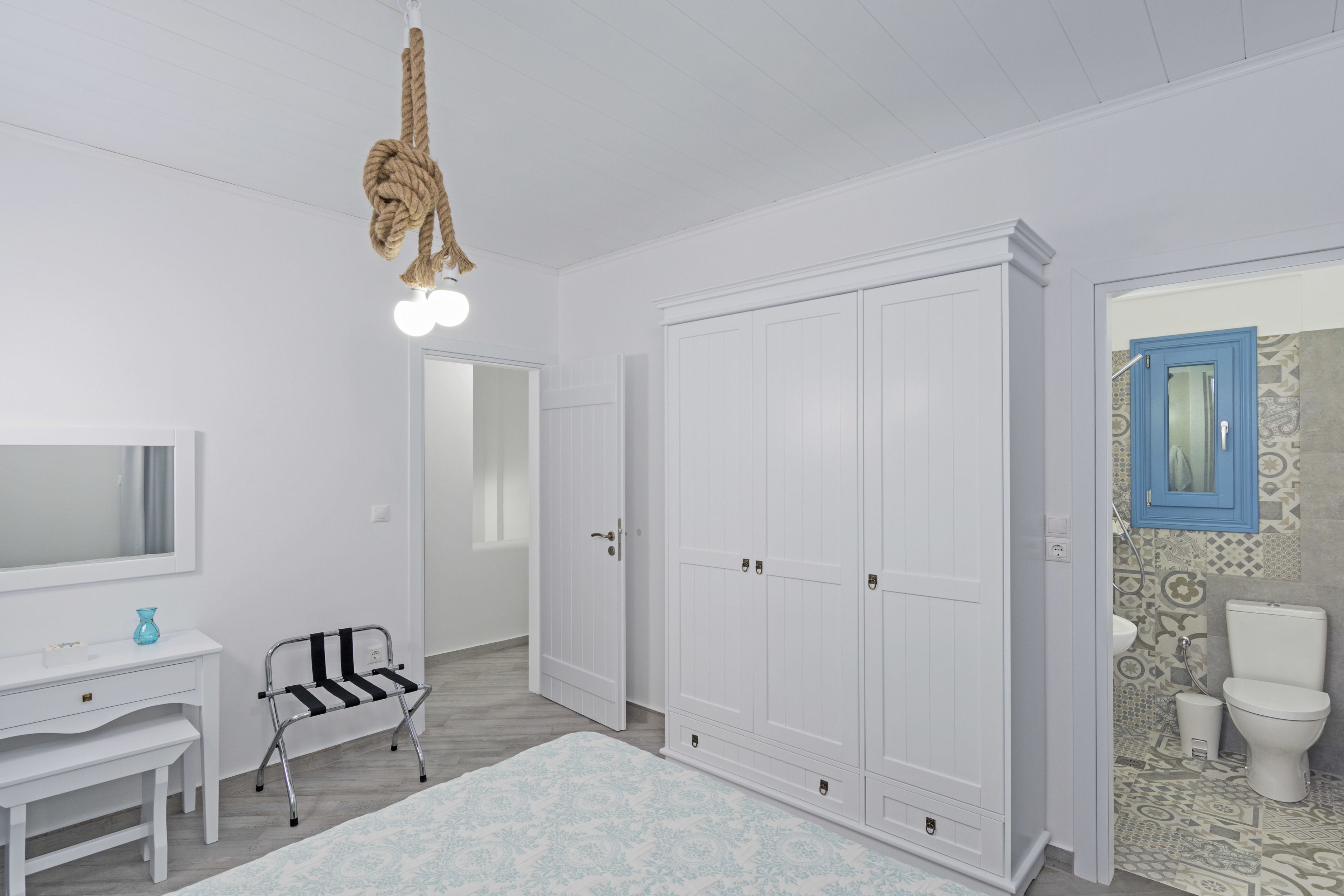 Un baño blanco con tocador blanco, una silla blanco y negro, y un amplio armario blanco.
